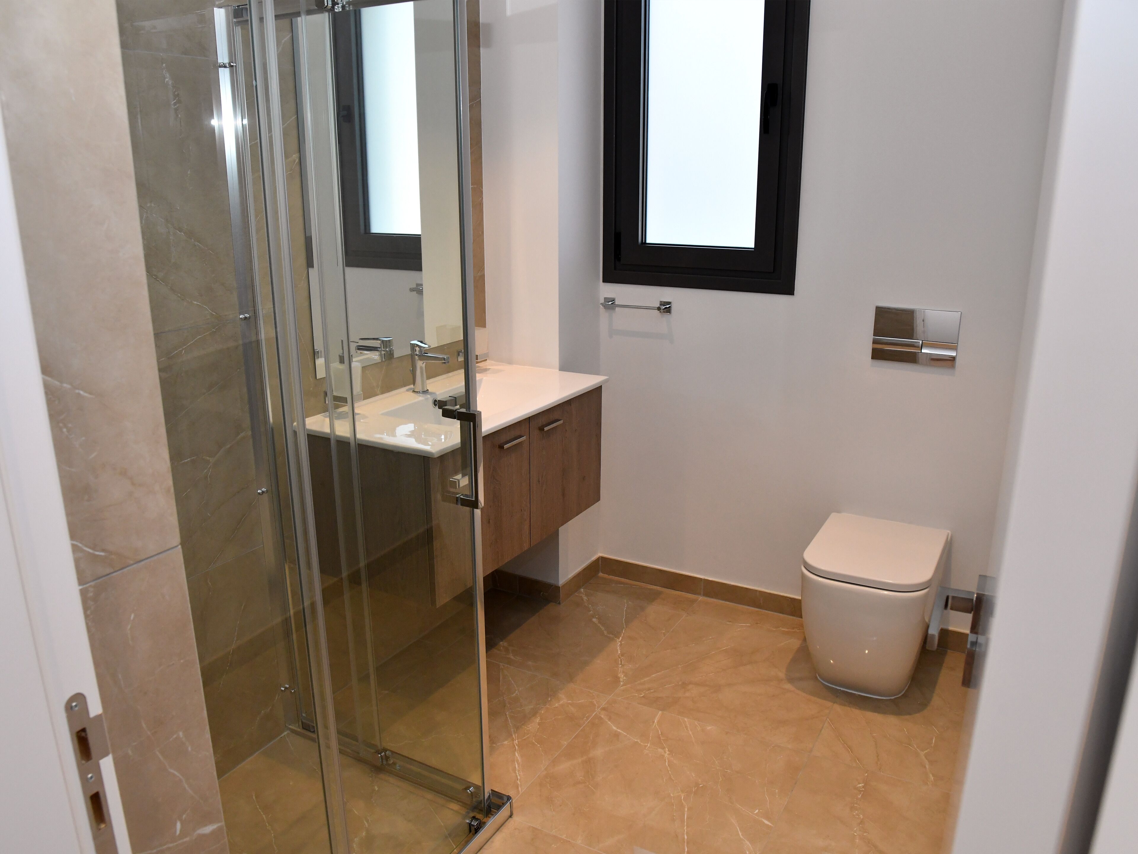 A bathroom with a glass shower enclosure, a sink with a mirror, a toilet, and a window above the sink.
