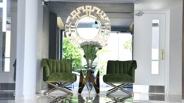 Um hall moderno com dois poltronas verdes, uma mesa de vidro e um espelho decorativo.