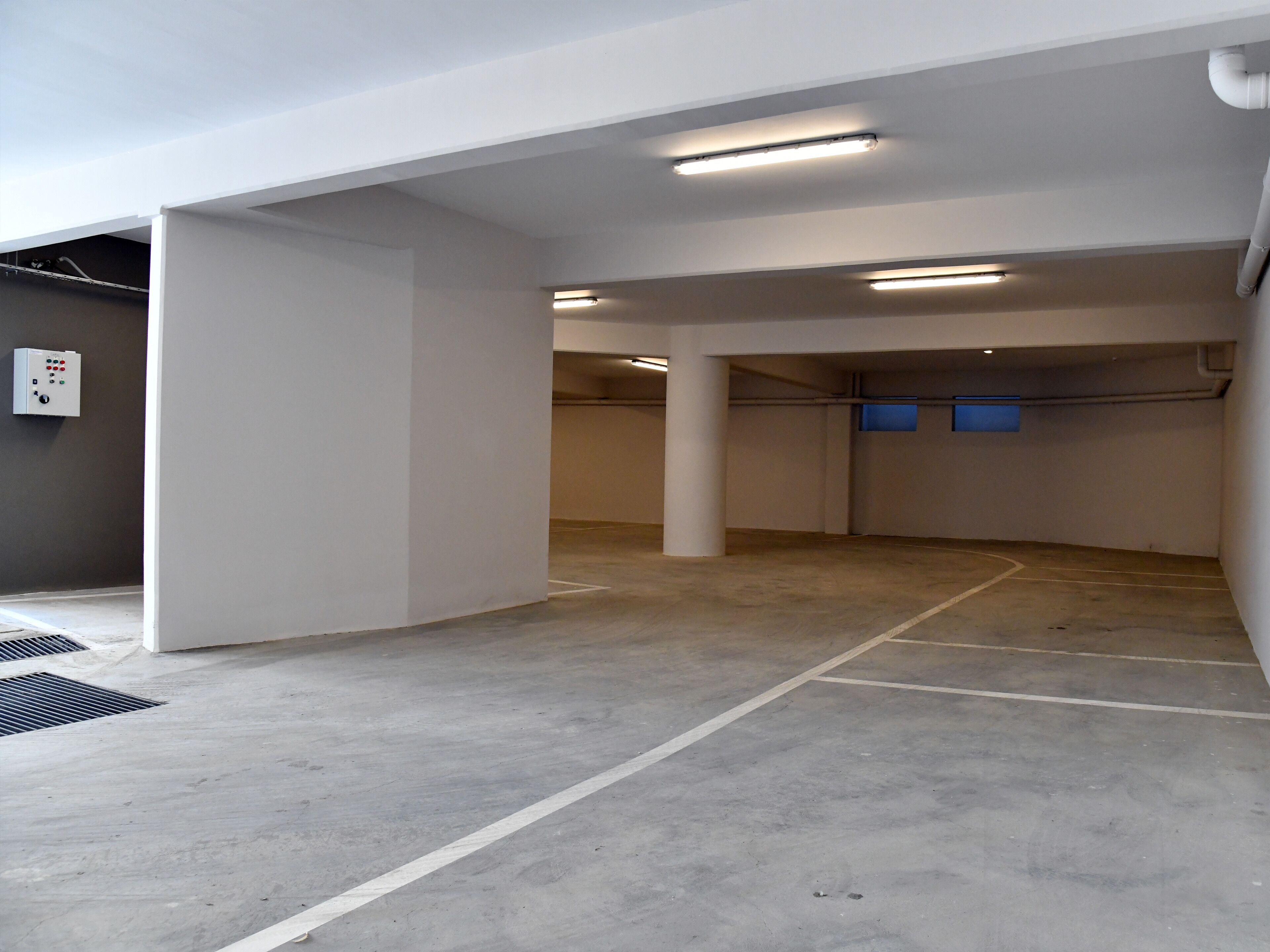 A parking garage with concrete floors and white walls, featuring several columns and overhead lighting.