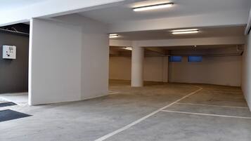 Een parkeergarage met betonnen vloeren en witte muren, met meerdere kolommen en verlichting aan het plafond.
