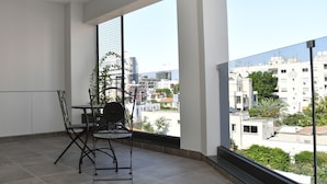 Uma varanda com mesa e cadeiras, um vaso de planta e vista para a paisagem urbana.