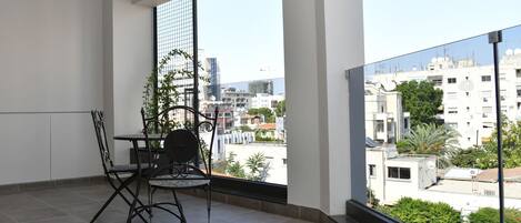 Un balcón con mesa y sillas, una planta en maceta y vistas de la ciudad.