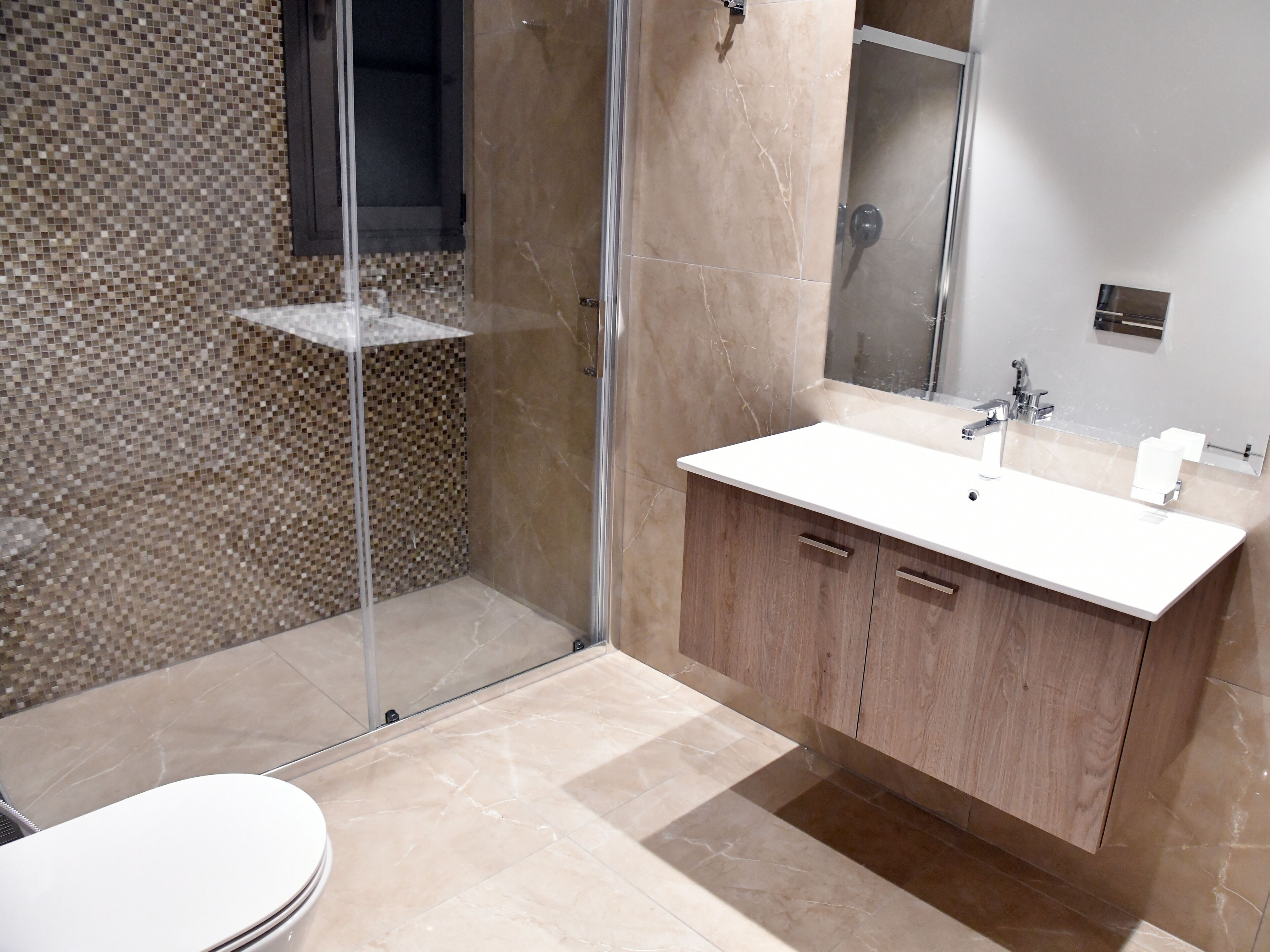 Un baño moderno con ducha envuelta en vidrio, un lavamanos blanco y un mueble de tocador de madera.