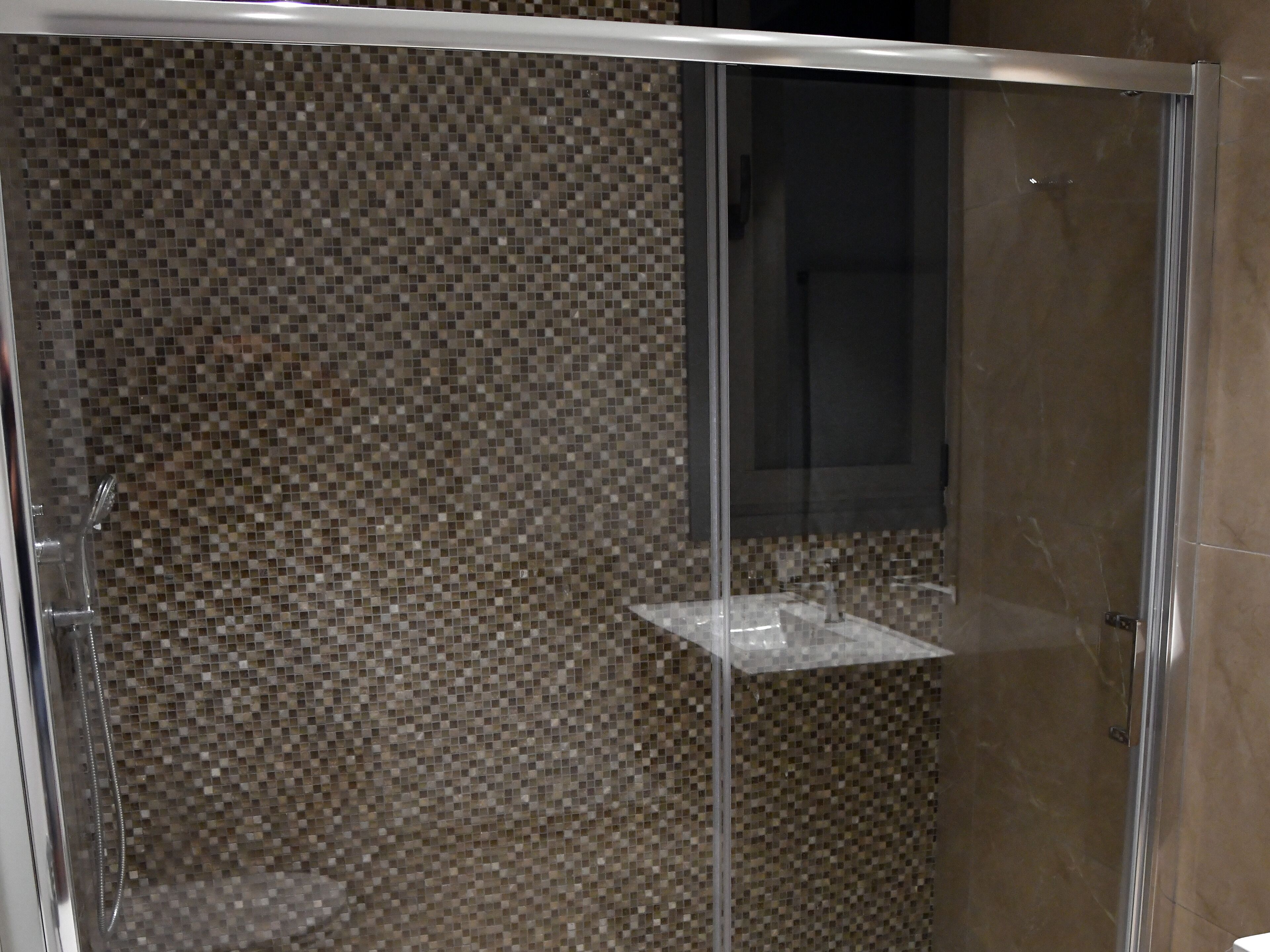 Una ducha con cerramiento de vidrio y pared de mosaicos.