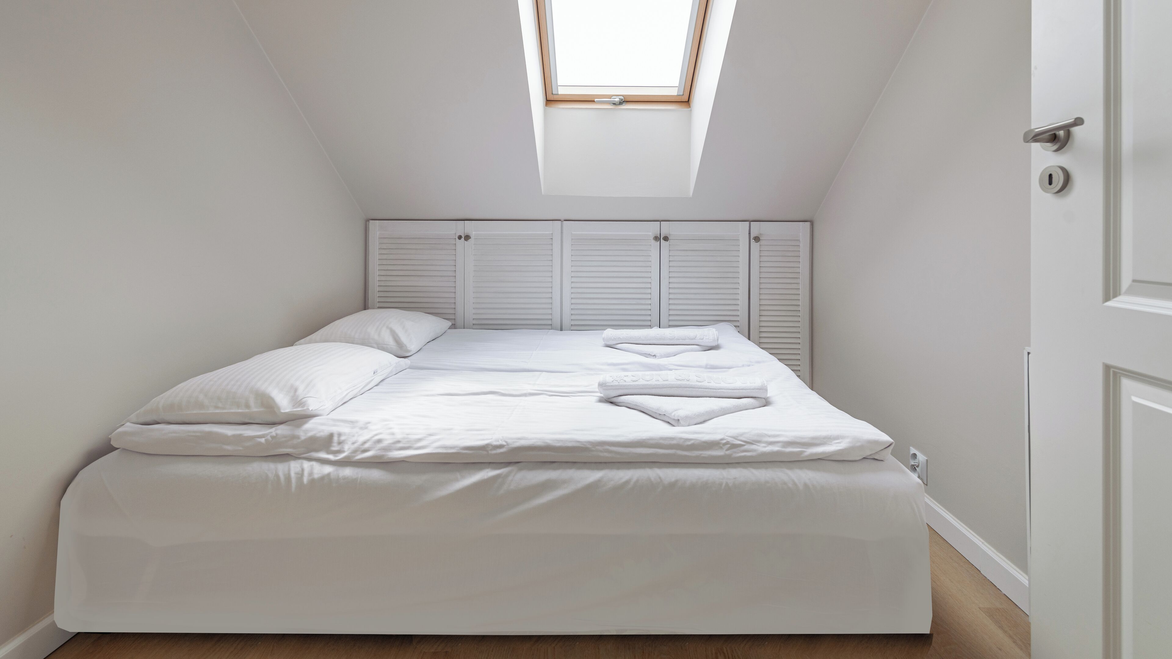 Un dormitorio con tragaluz, ropa de cama blanca y suelo de madera.