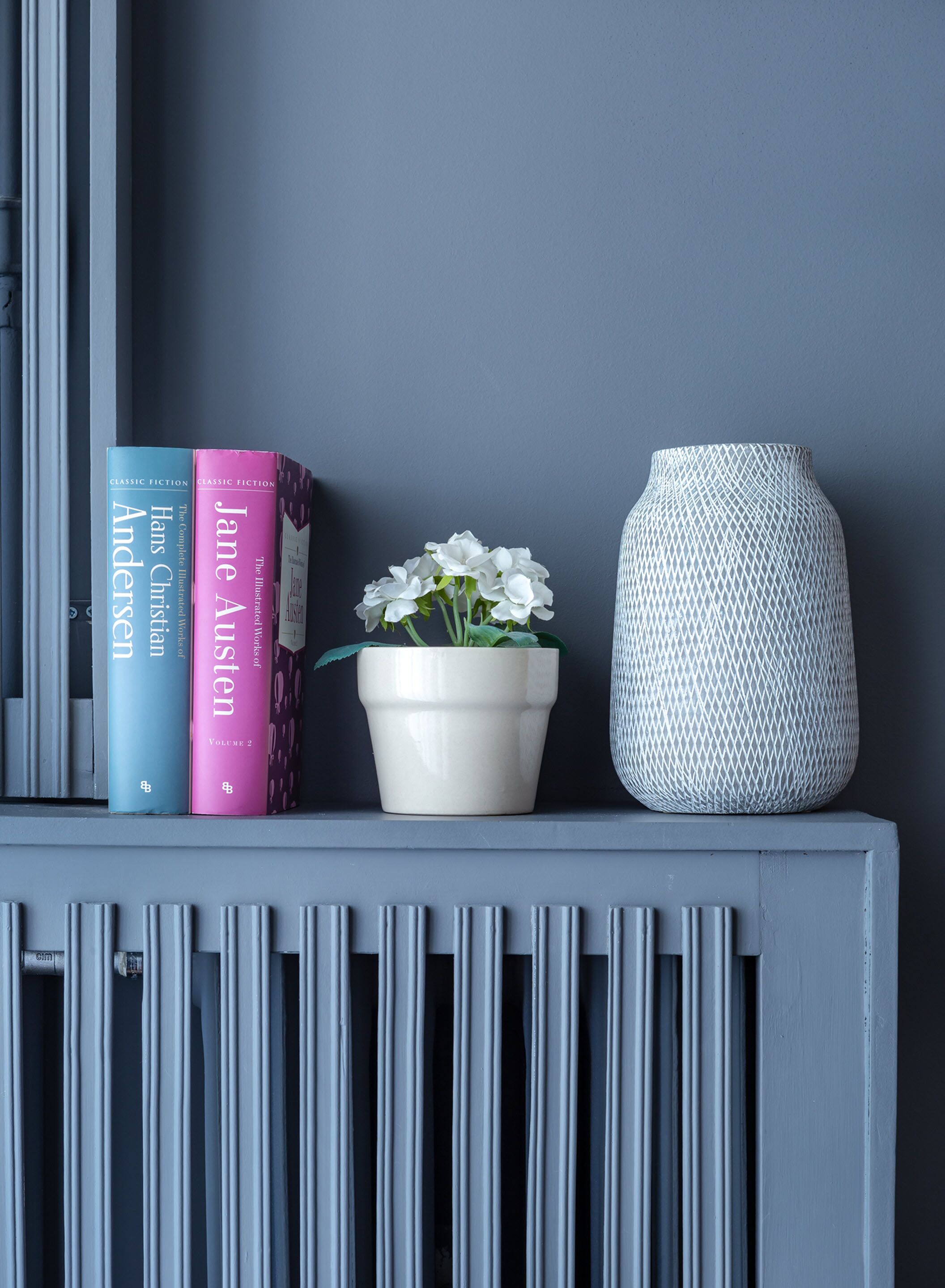 A shelf with books, a potted plant, and a vase.