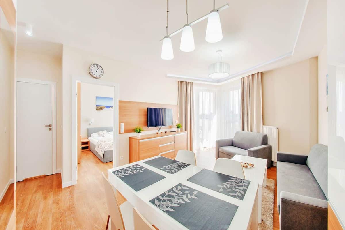 A modern living room with a dining area, a television, and a clock on the wall.