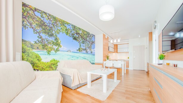 Een moderne woonkamer met een grote strandmuur, een bank, een salontafel en een keukenhoek met houten kasten en een televisie.