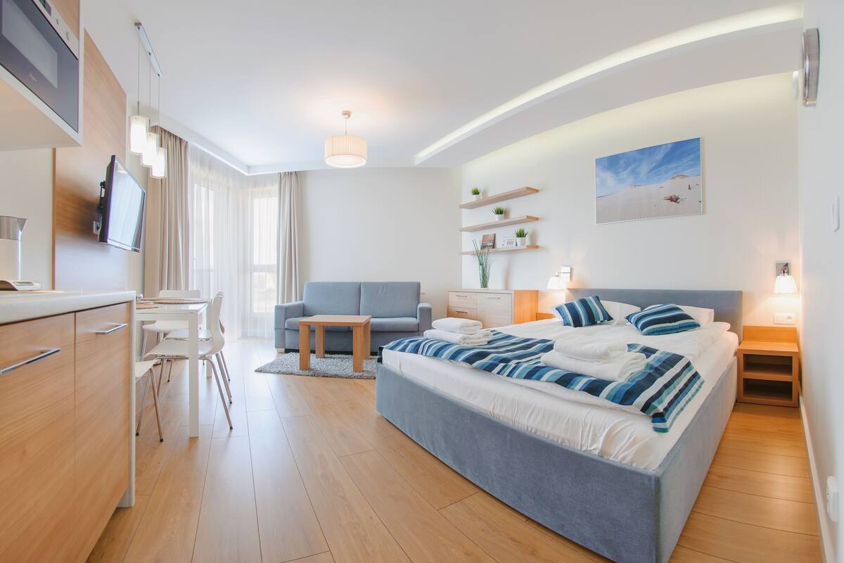 A modern hotel room with a large bed, a desk, a sofa, and a TV.