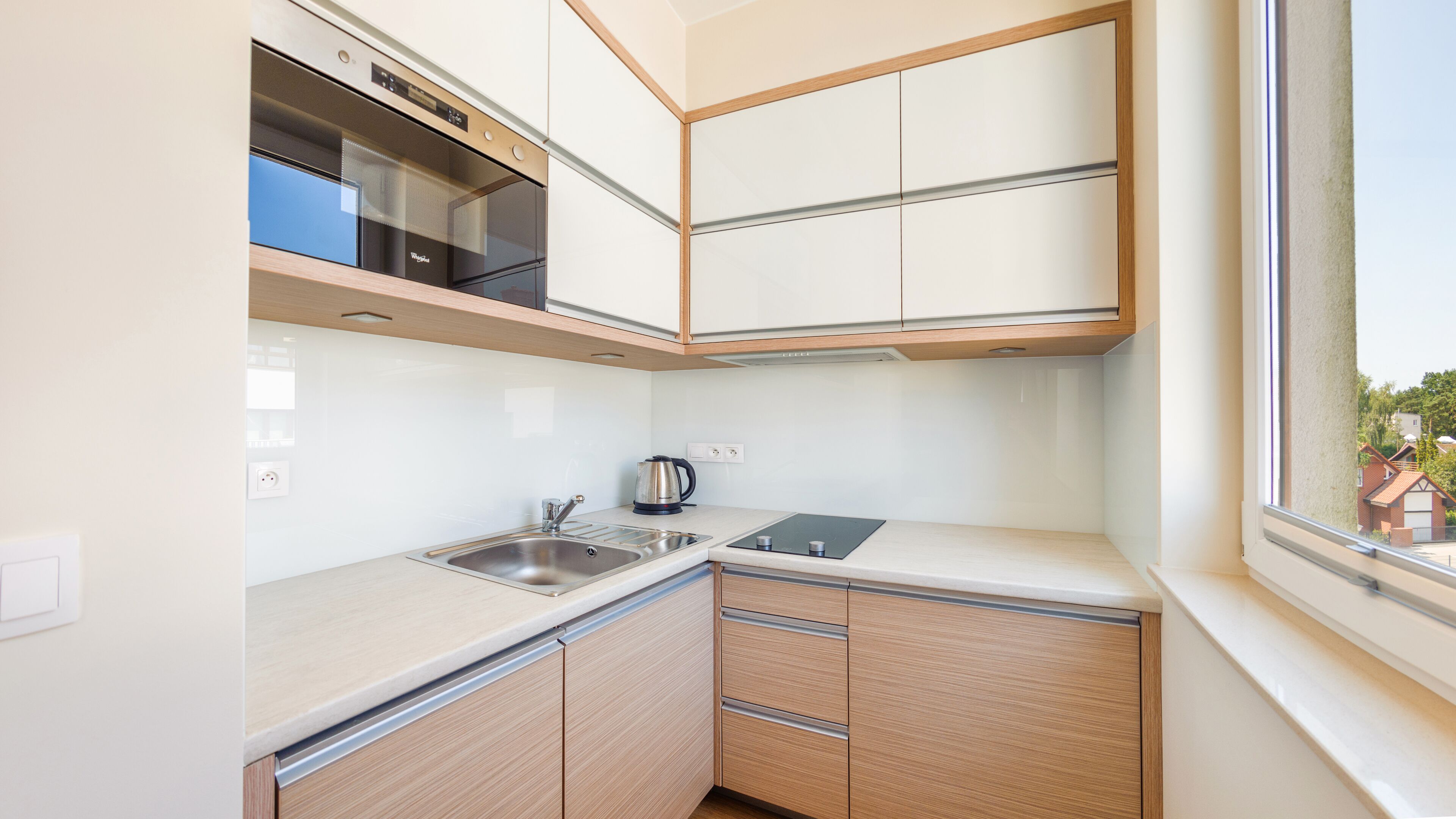 Cocina compacta con un lavamanos de acero inoxidable, un hervidor y armarios de madera.