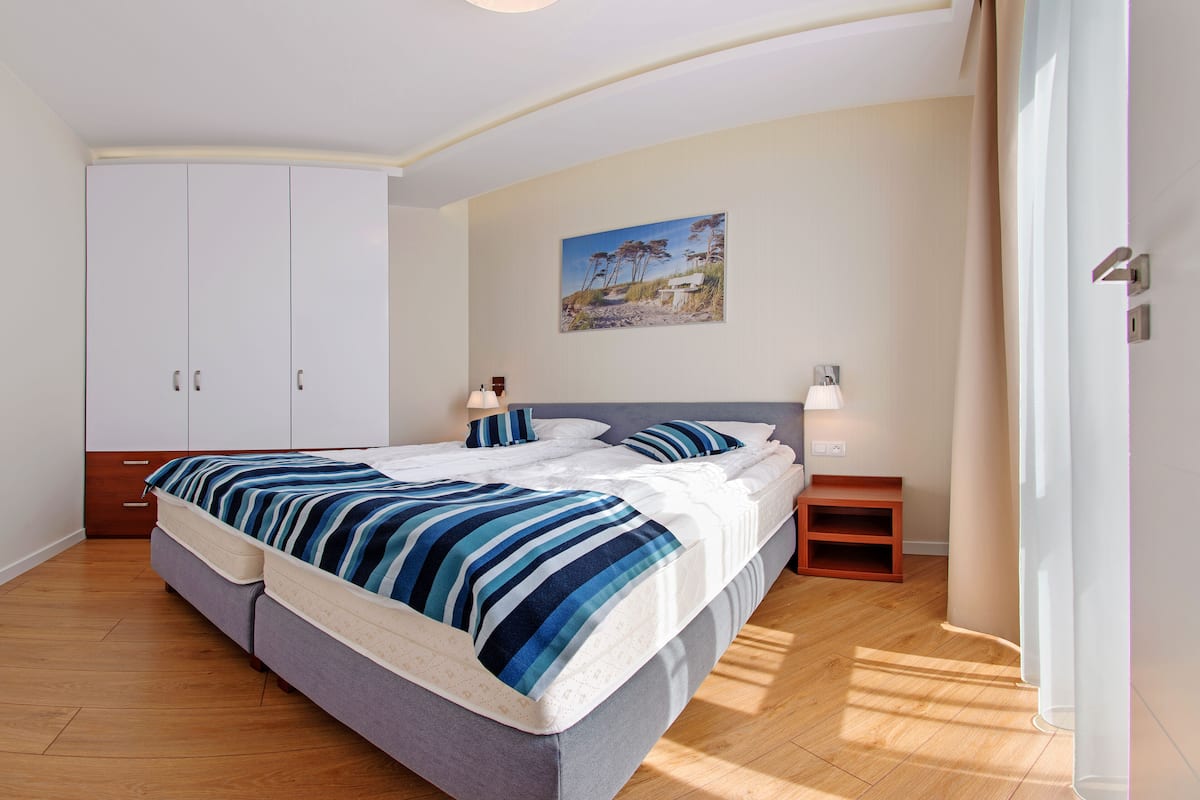 A bedroom with a bed, a nightstand, a lamp, a painting on the wall, and a wardrobe.