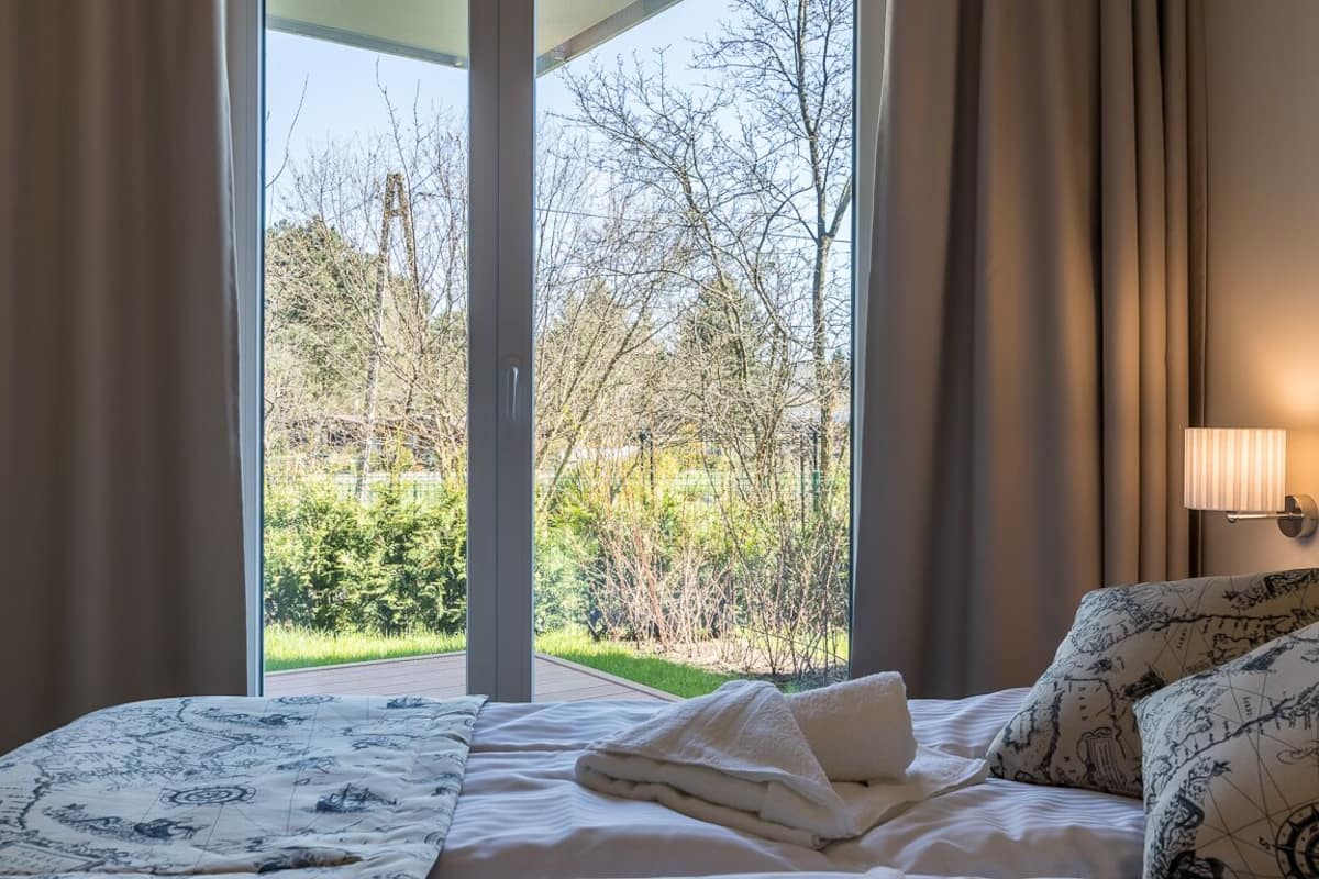 A hotel room with a bed, a window with curtains, and a view of trees and greenery outside.