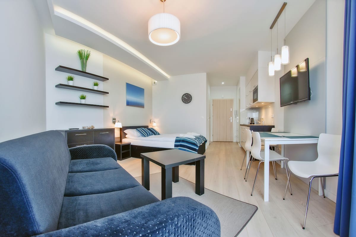 A modern living room with a sofa, a dining table, and a TV mounted on the wall.