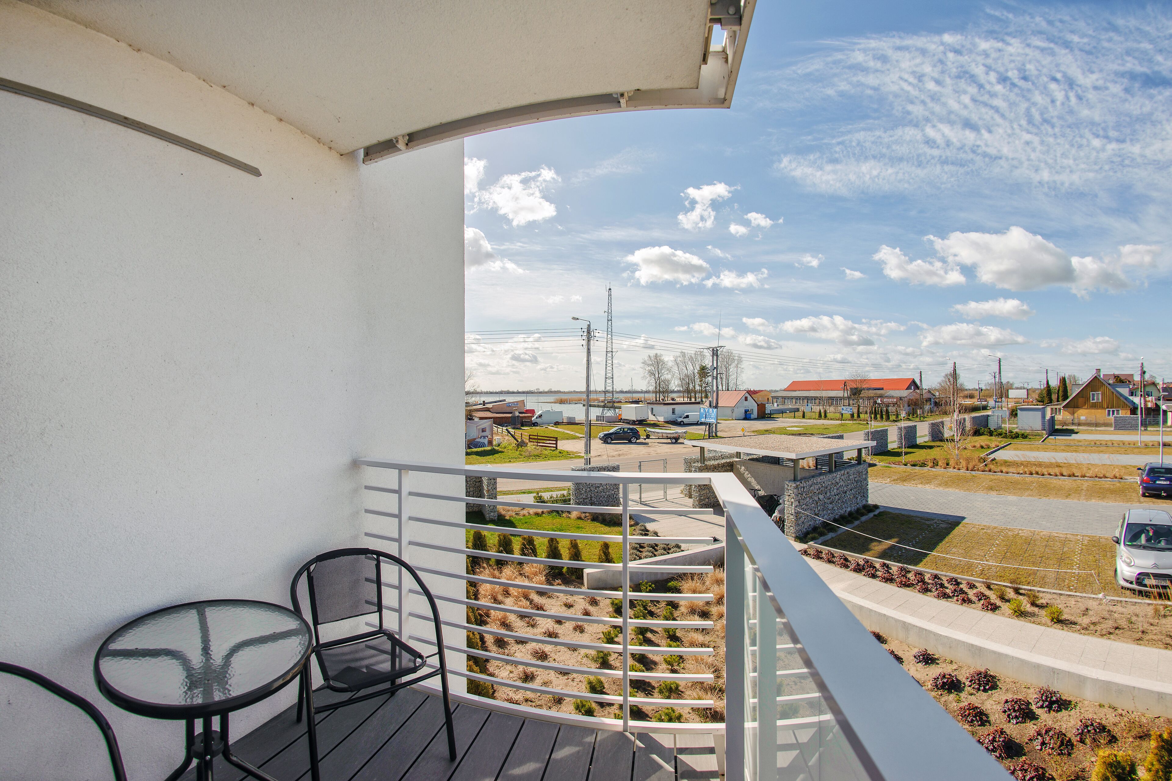 Ein Balkon mit Glastisch und Stühlen, mit Blick auf einen Parkplatz und Gebäude.