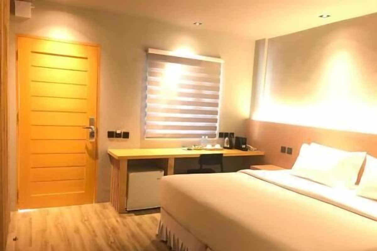 Habitación de hotel con cama, escritorio, silla, mesita, ventana con persianas y puerta.