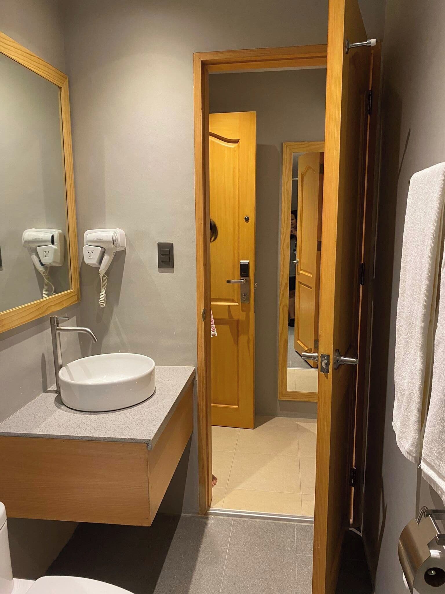 A bathroom with a sink, two hair dryers, a mirror, and a wooden door leading to another room.