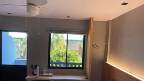 A hotel room with a bed, a desk with a computer, a small kitchenette, a window with a view of greenery, and a ceiling fan. - Mayfair Resort (Panglao)