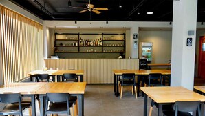 A modern cafe interior with wooden tables and chairs, a bar area with shelves of beverages, and a ceiling fan. - Mayfair Resort (Panglao)