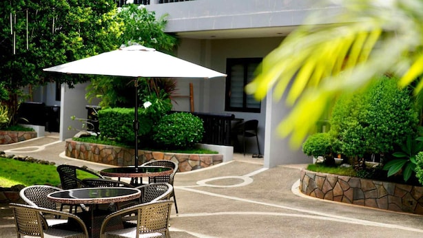 An outdoor seating area with wicker tables and chairs, surrounded by greenery and a stone wall. - Mayfair Resort (Panglao)