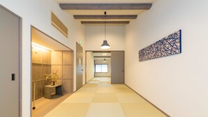Un couloir doté d’un sol à carreaux, d’un luminaire suspendu, d’une œuvre d’art abstraite accrochée au mur et d’un banc sur lequel est posé un vase de fleurs.