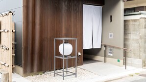 Une entrée moderne, avec un mur composé de lambris en bois, une structure métallique surmontée d’un objet sphérique et un rideau blanc.