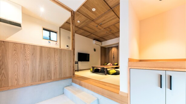 A modern interior with a wooden ceiling, a flat-screen TV, a dining area with a table and chairs, and a staircase leading to another level. - Musubi Hotel Machiya Naraya-machi 2 (Fukuoka)