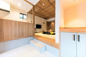 A modern interior with a wooden ceiling, a flat-screen TV, a dining area with a table and chairs, and a staircase leading to another level. - Musubi Hotel Machiya Naraya-machi 2 (Fukuoka)