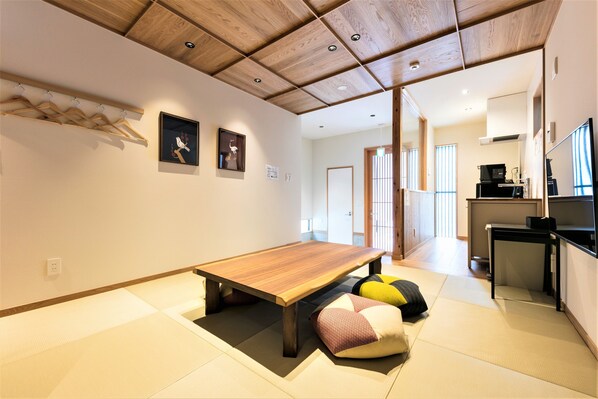 Una sala de estar moderna con una mesa de madera, esteras de tatami y una cocina visible al fondo.