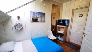 A room with a bed, a chair, a TV, and a door. - Meridian Apartments (Klaipeda)