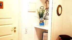 A hallway with a white door, a small shelf with a plant, a framed certificate, and a mirror with a decorative wreath. - Meridian Apartments (Klaipeda)