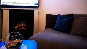 A living room with a flat-screen TV mounted above a fireplace, a sofa with cushions, and a glass bowl on a coaster on a table. - Meridian Apartments (Klaipeda)