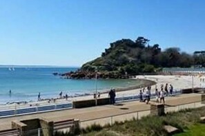 A coastal promenade with a sandy beach, a rocky outcrop, and a clear blue sky. - Trébeurden Beach T3 (Accommodation close to the beach and GR 34) (Trébeurden)