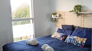 A bedroom with a large bed, a bedside table, a hanging plant, and a view of the outdoors. - Trébeurden Beach T3 (Accommodation close to the beach and GR 34) (Trébeurden)
