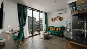 Una sala de estar moderna con un sofá verde, una mesa de centro y un televisor. Hay un balcón con vistas a edificios.