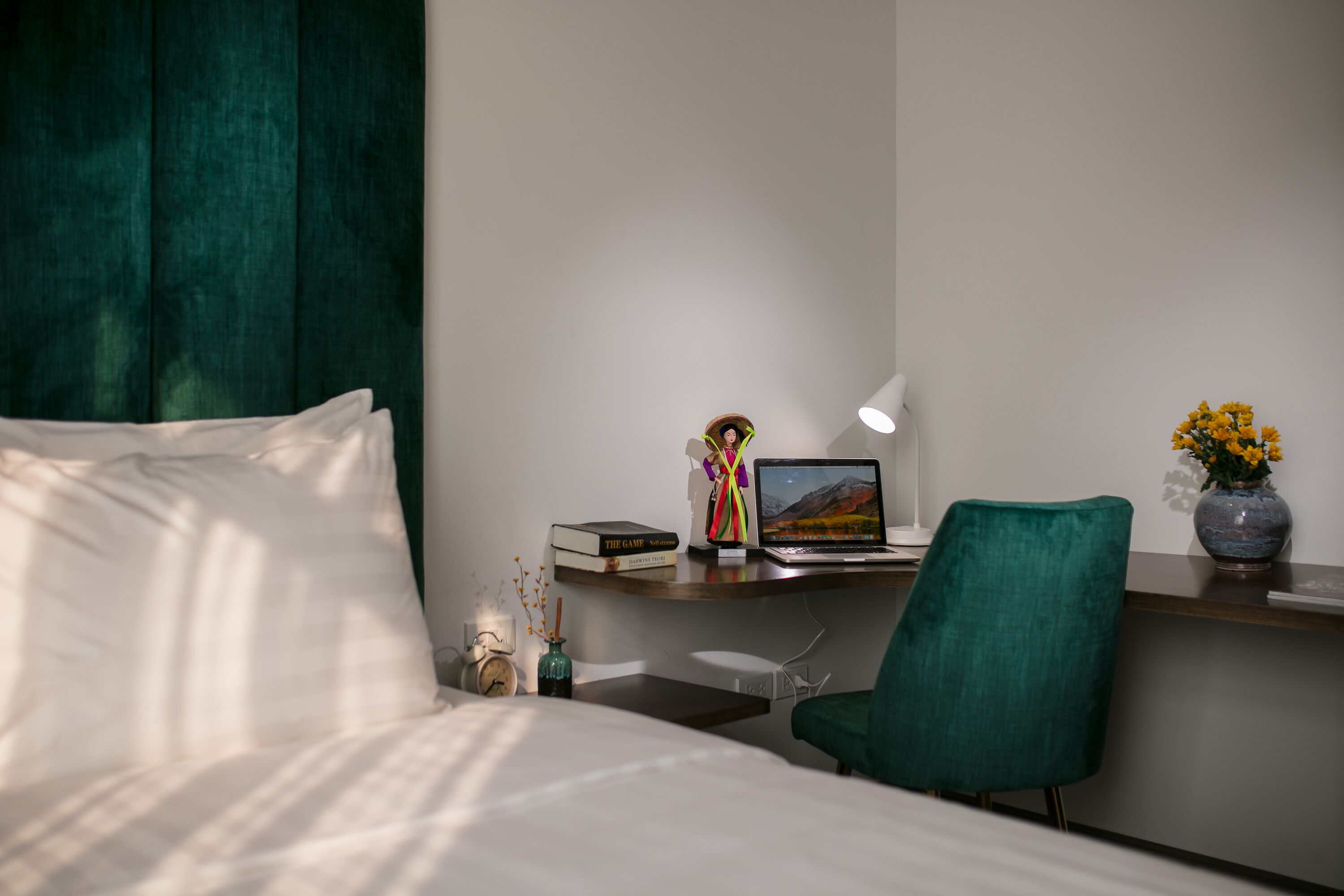 Habitación de hotel ordenada con una cama, un escritorio con una computadora portátil, una silla y un florero con flores.