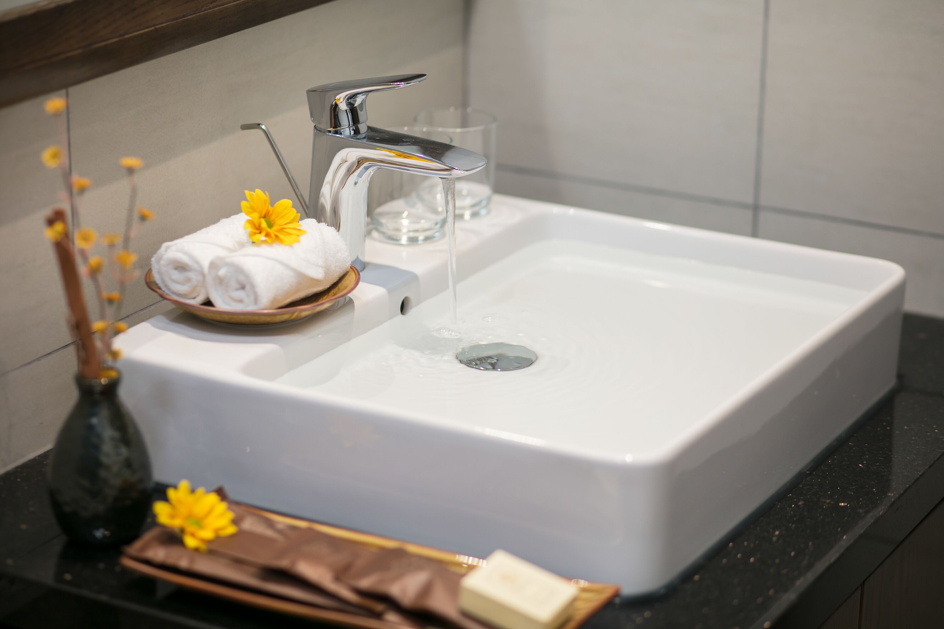 A bathroom sink with a towel and flowers, a glass of water, and toiletries on the counter.