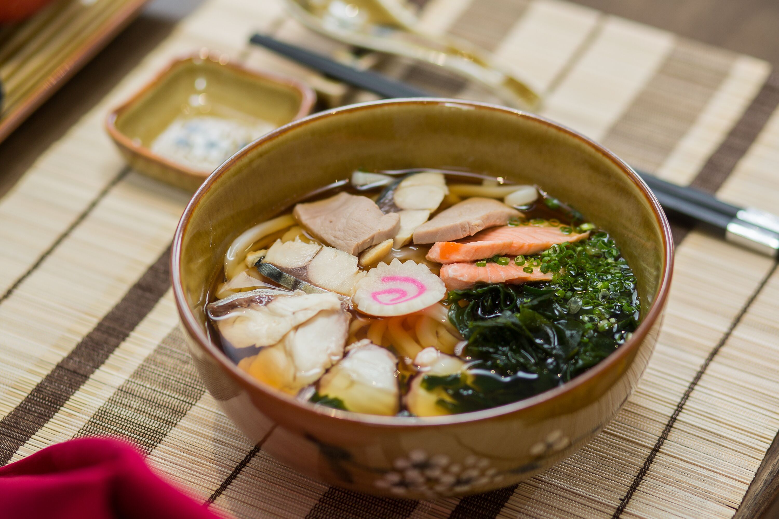 Eine Schüssel Suppe mit verschiedenen Zutaten auf einer gewobenen Matte.