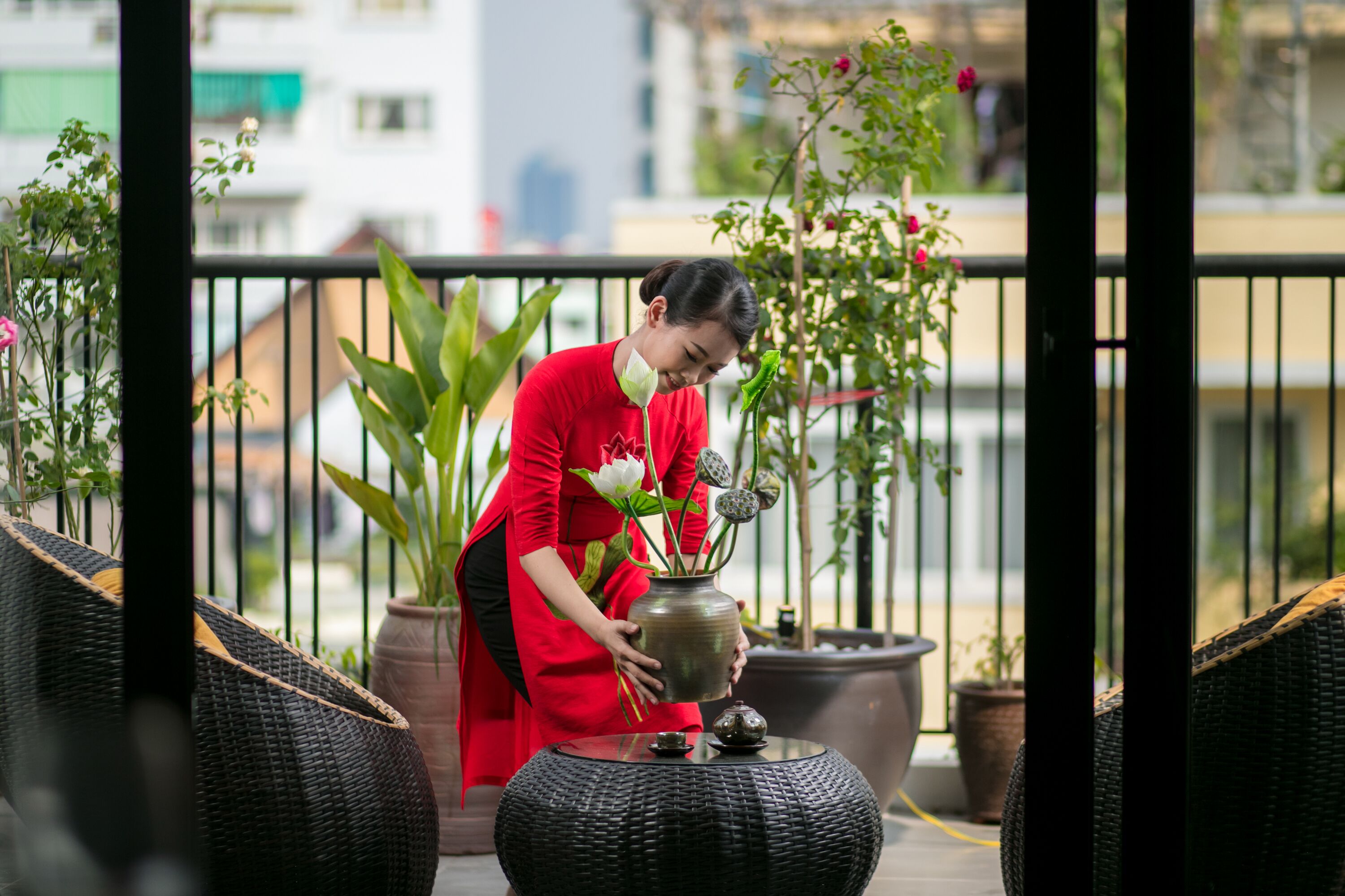 A person in a red outfit arranging a vase with flowers on a round table outdoors.