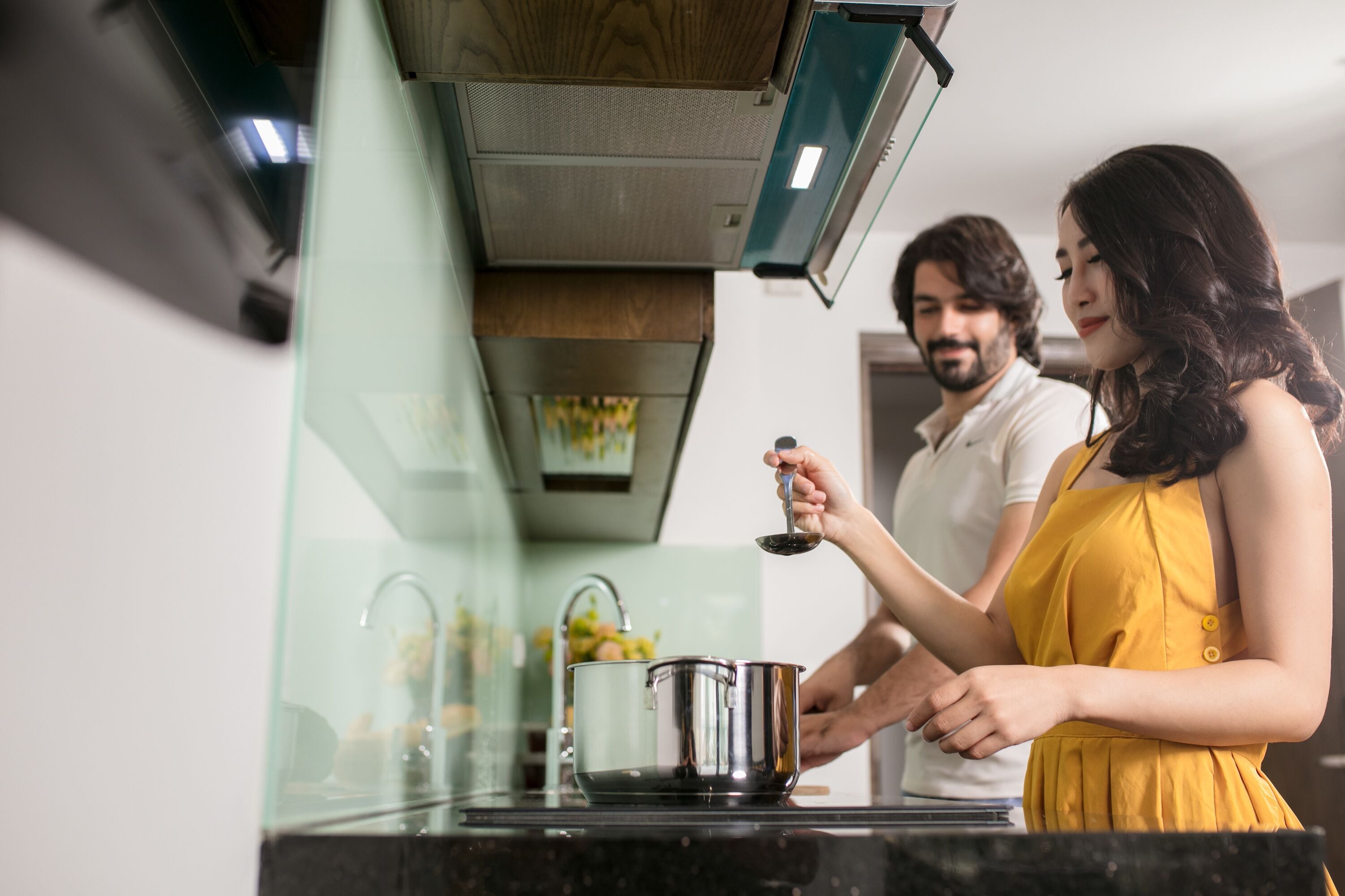 A modern kitchen with a stainless steel stove, a glass backsplash, and a person holding a wine glass.