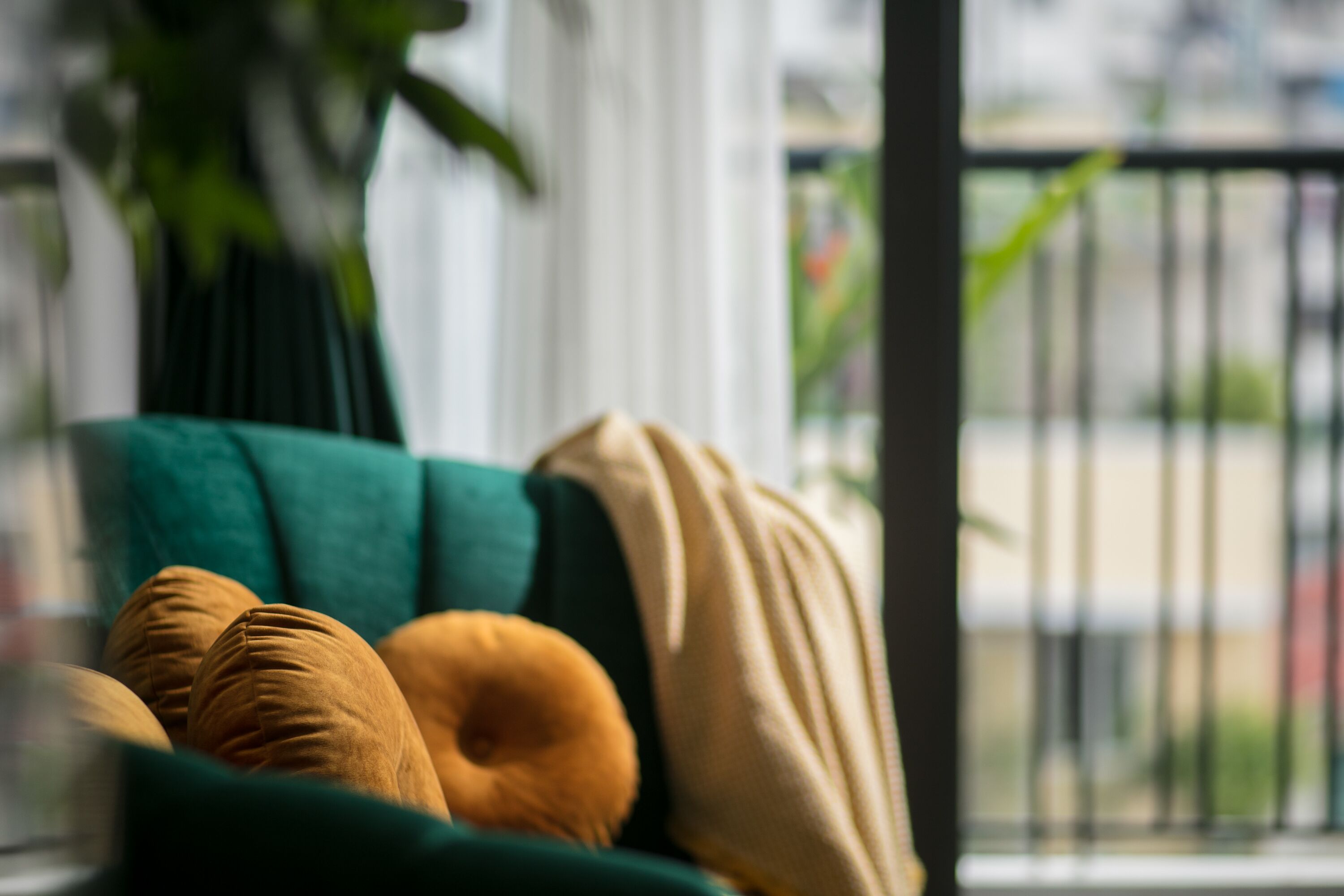 Un sofá verde con una manta color beige y dos almohadas amarillo mostaza.