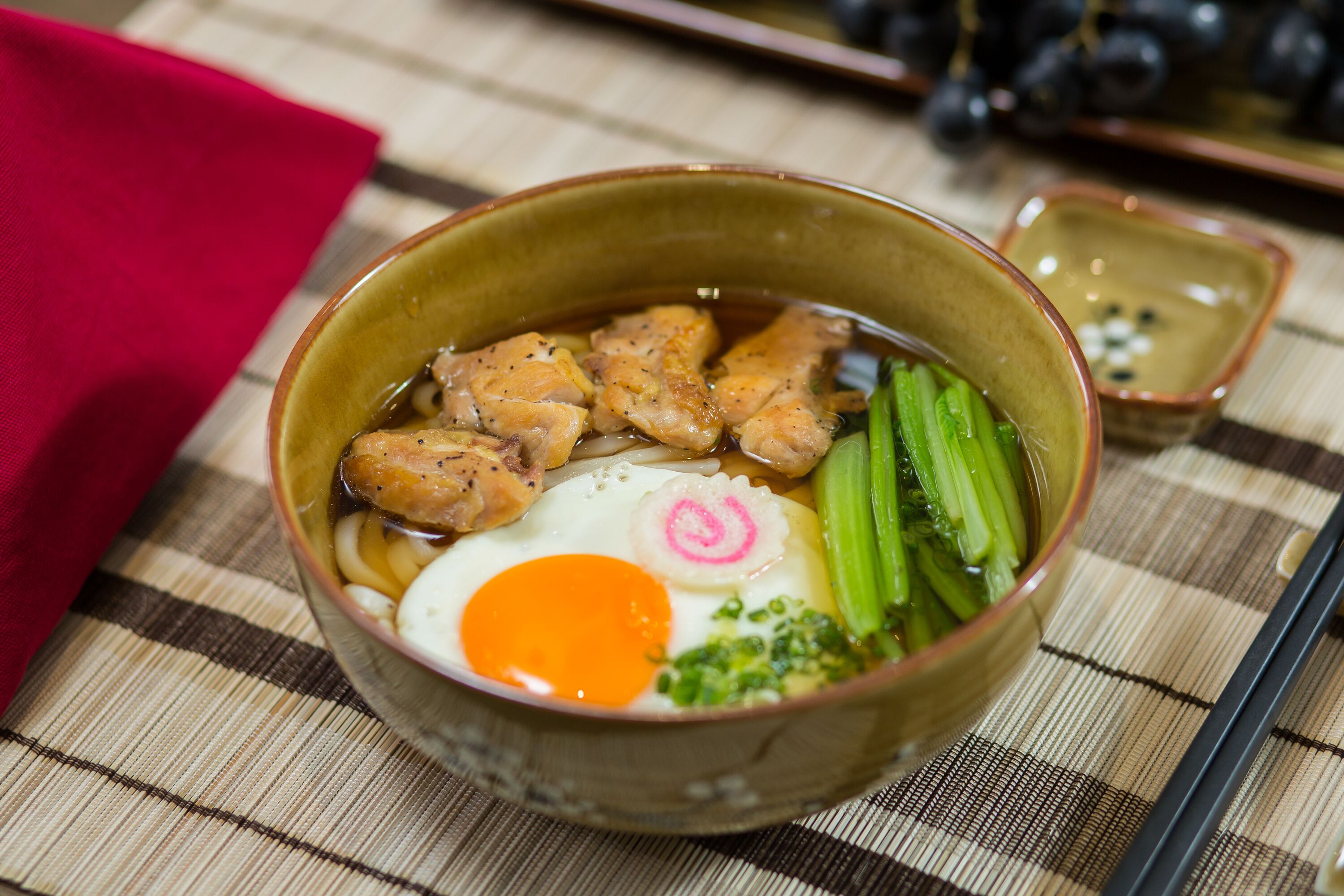 A bowl of ramen with various toppings including egg, green vegetables, and meat.
