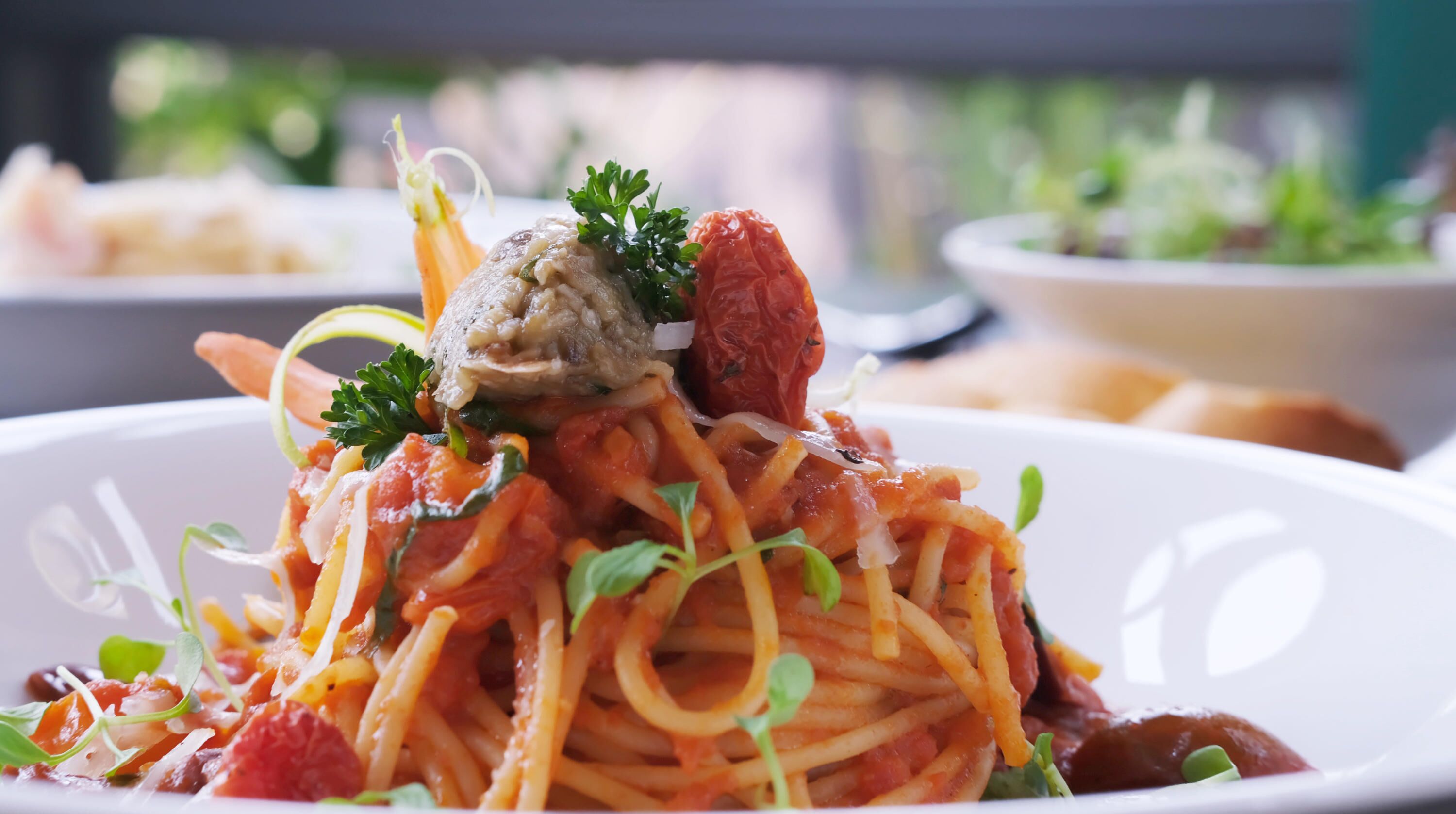 Eine Spaghetti-Portion mit einer Hackfleakugel, Tomatensauce und Garnitur.