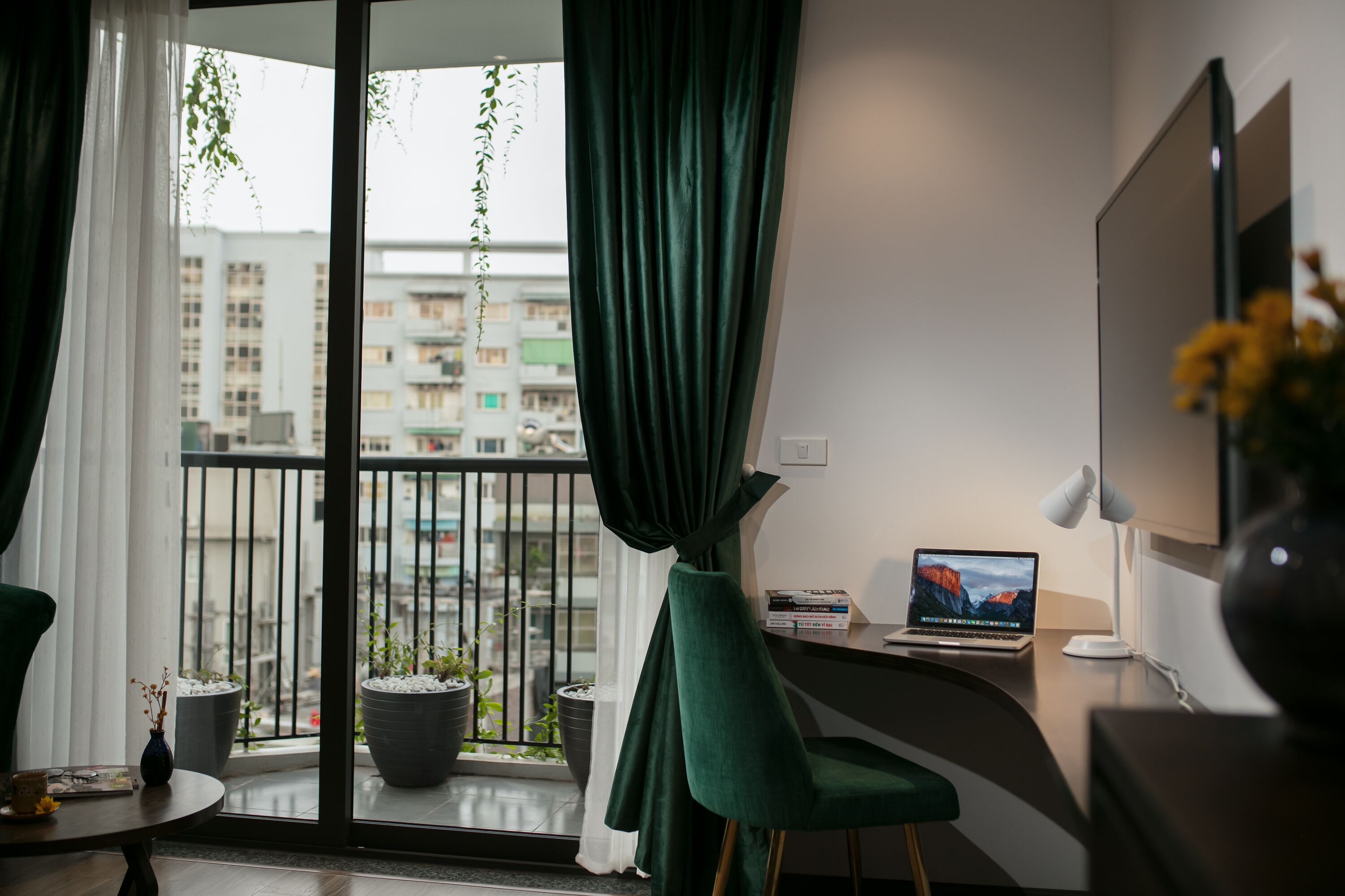 Une chambre moderne avec une grande fenêtre, un bureau avec un ordinateur portable, une chaise et une plante en pot.
