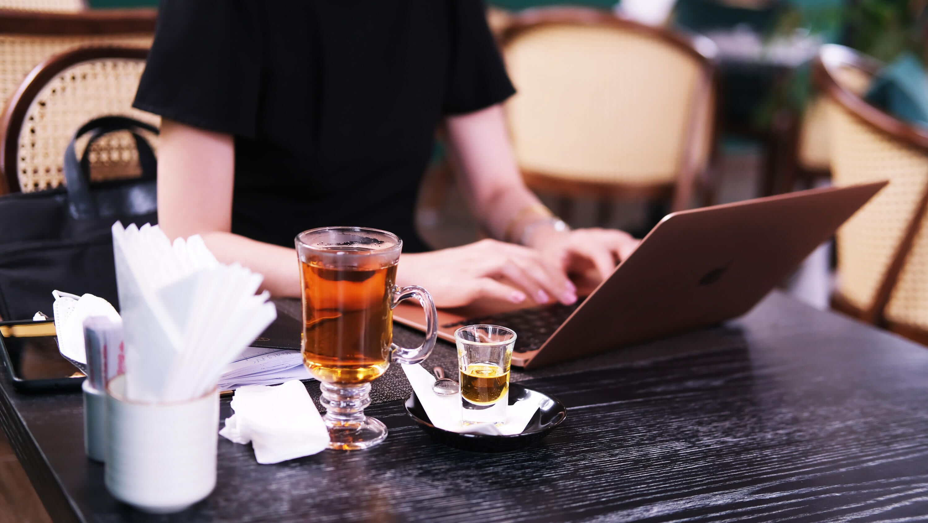 Una laptop sobre una mesa con una taza de té y un vaso pequeño.