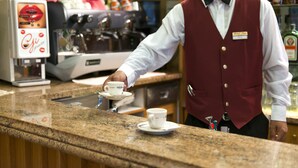 A barista serving coffee at a counter with an espresso machine in the background. - Hotel Iris (Roccaraso)