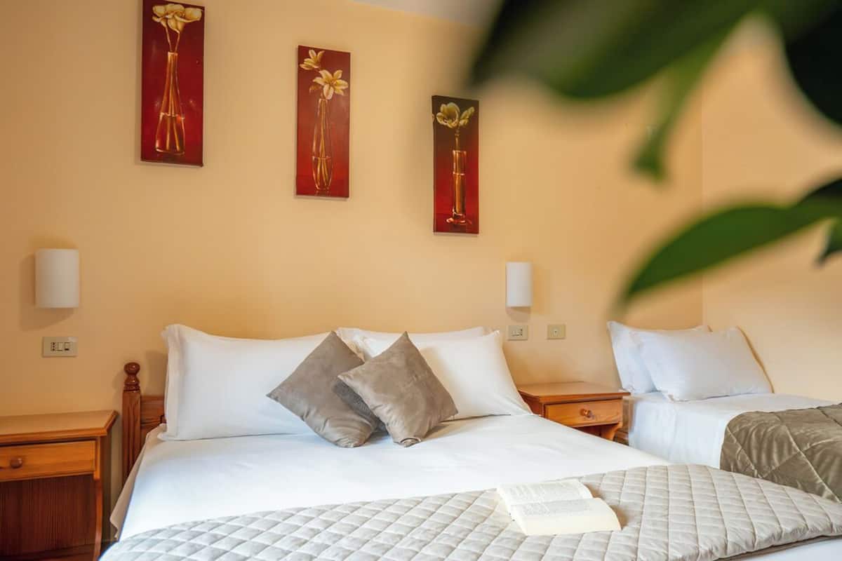 A hotel room with a bed, two nightstands, and wall-mounted lamps.