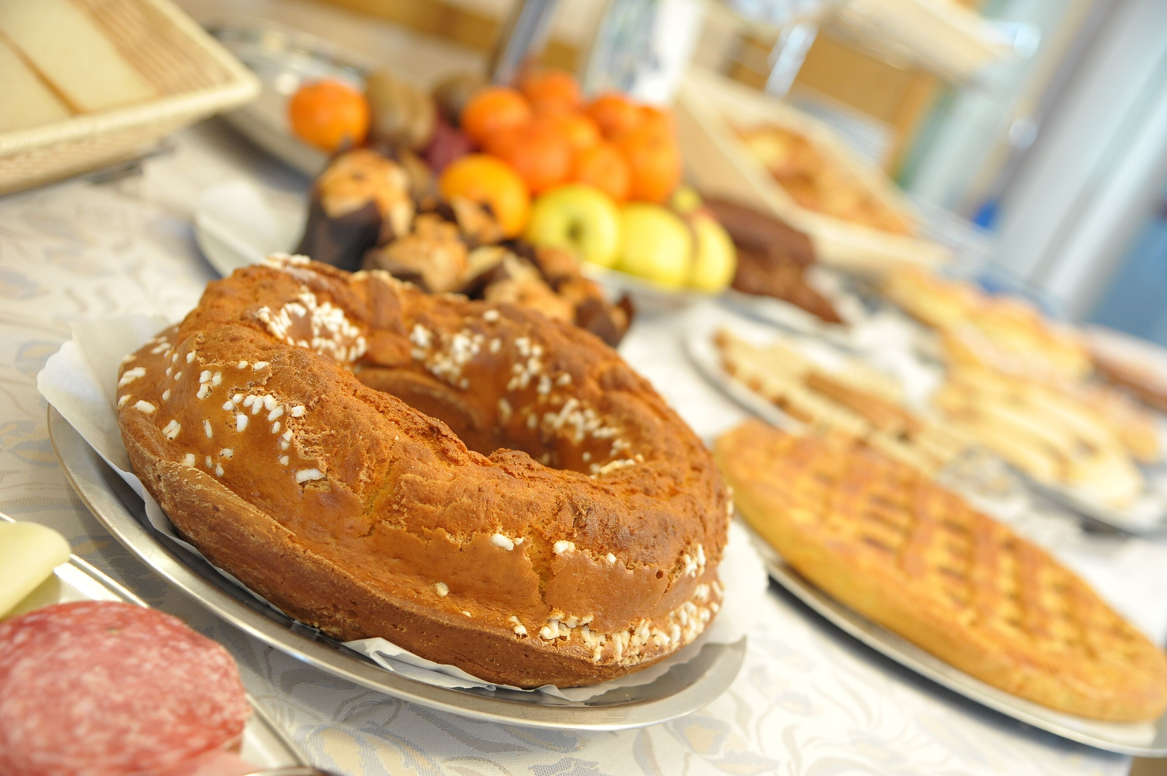 A table with various food items including a ring-shaped bread, pastries, and a selection of fruits and vegetables.