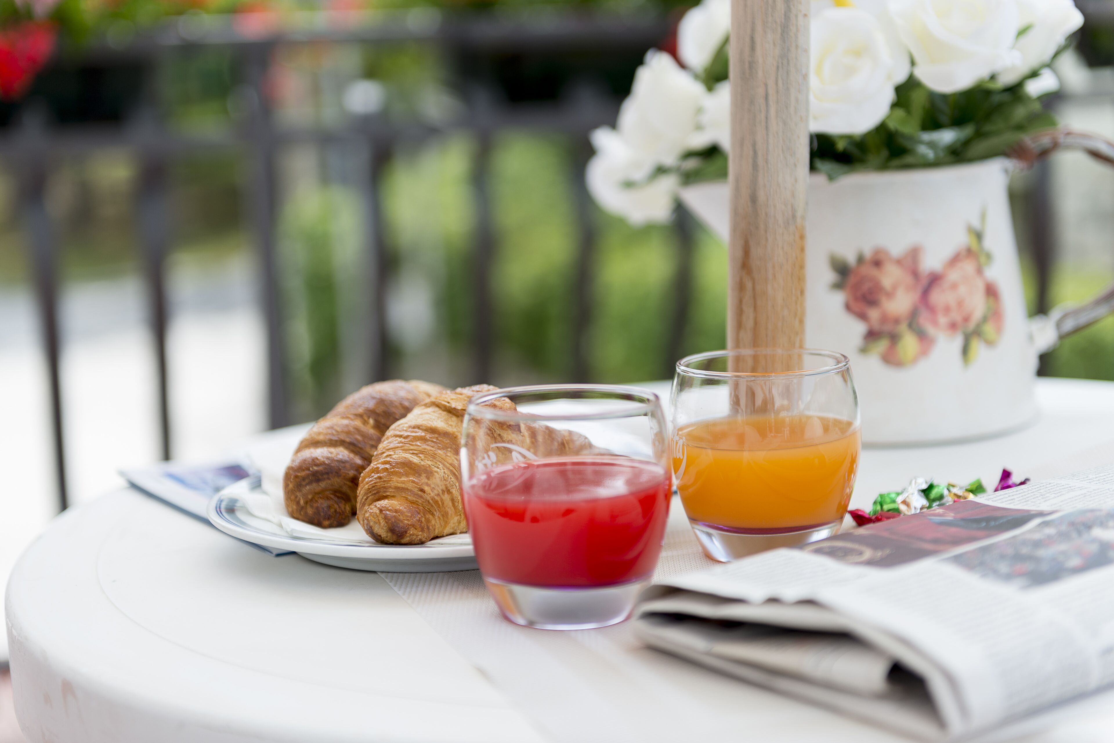 Una colazione con croissant, un bicchiere di succo di mirtilli rossi e un bicchiere di succo d'arancia su un tavolo con un giornale.