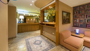 A hotel lobby with a reception desk, a floral arrangement, a painting, and a patterned rug. - Hotel Iris (Roccaraso)
