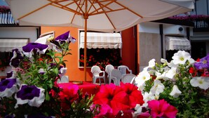An outdoor seating area with a white umbrella, white chairs, and a table with a red tablecloth. - Hotel Iris (Roccaraso)